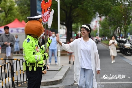 6月7日上午9時，隨著鈴聲的響起，2023年江西高考正式開考，江西省的53.57萬考生以縣（區(qū)）為單位隨機安排在全省256個考點、18968個考場參加高考。圖為“小熊交警”和考生擊掌鼓勵。 人民網(wǎng)記者 時雨攝