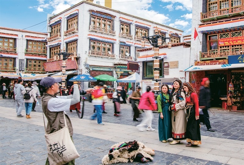 千年八廓街，見證民族團(tuán)結(jié)。2021年7月，習(xí)近平總書記來(lái)到位于西藏拉薩老城區(qū)的八廓街，感慨地說(shuō)：“千年八廓街，是我們各民族建起來(lái)的八廓街。各民族文化在這里交流交往交融，我們中華民族的大家庭在這里其樂(lè)融融。”圖為2023年6月13日，游客身著藏裝在八廓街拍照留念。 新華社記者 姜帆/攝