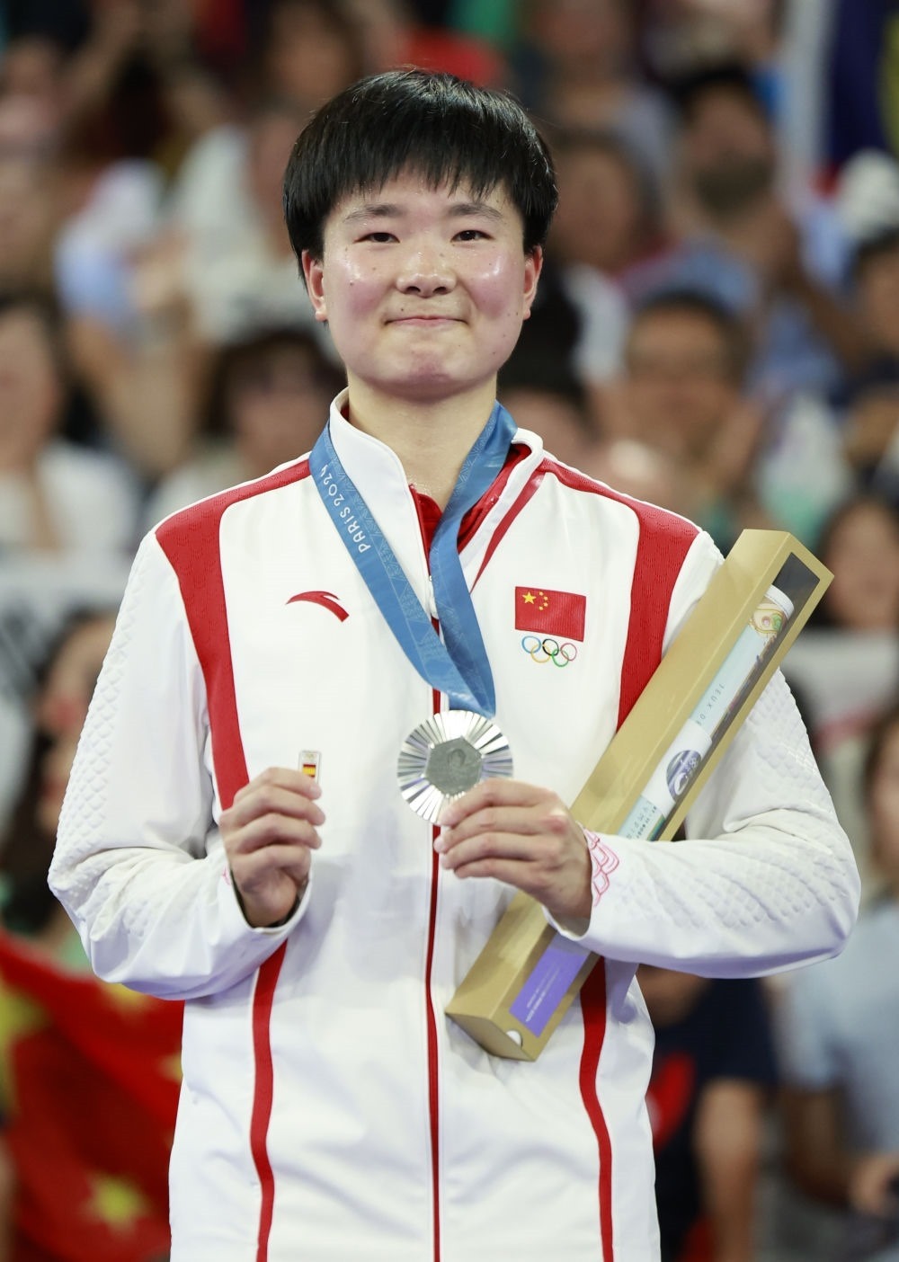 巴黎奧運(yùn)會(huì)羽毛球女子單打亞軍、中國(guó)選手何冰嬌在頒獎(jiǎng)儀式上一手握著銀牌，一手握著西班牙奧委會(huì)徽章（2024年8月5日攝）。新華社記者 任正來(lái) 攝